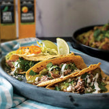 Chili Verde Pork Carnitas tacos with homemade salsa verde made with Olivelle Pineapple Habanero White Barrel Aged Balsamic and Green Chili Infused Olive Oil, topped with cotija, crema, and lime