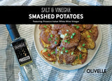 Crispy salt and vinegar smashed potatoes on a baking sheet drizzled with olive oil and seasoning