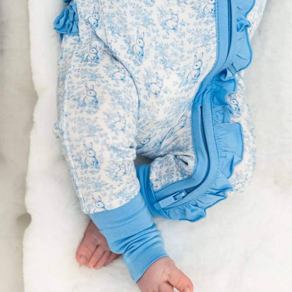 Baby in a blue and white floral outfit on a white blanket