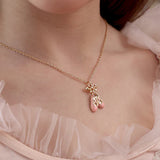 Necklace with a pink pendant worn by a person in a light pink outfit.