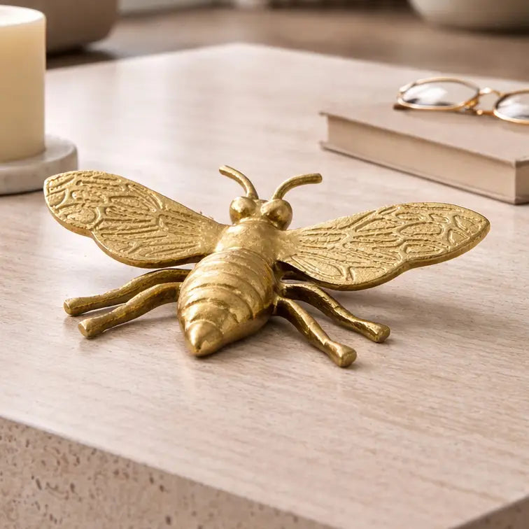 Gold bee figurine on a wooden surface with books and glasses in the background