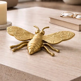 Gold bee figurine on a wooden surface with books and glasses in the background