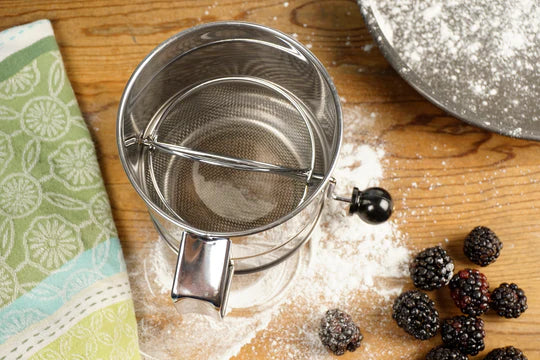 Metal strainer on a wooden surface with blackberries and flour