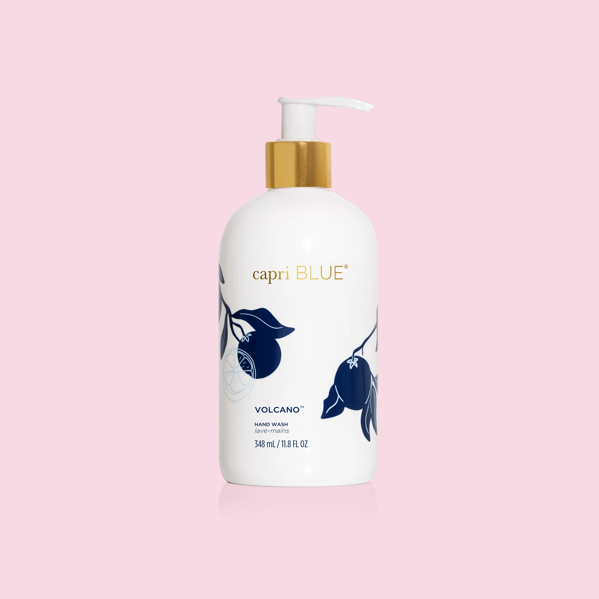 A white pump bottle of Capri Blue hand wash with blue floral illustrations and gold accents on a pink background.
