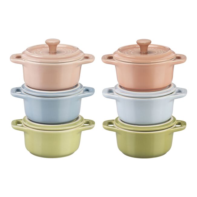 Set of four small ceramic pots with lids in pastel colors on a white background