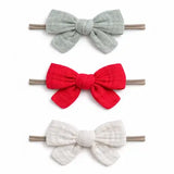 Three fabric bow hair clips in sage green, bright red, and off-white, arranged vertically on a plain white background.