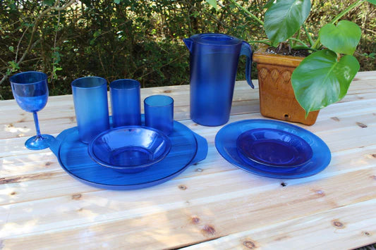 Blue plastic tableware set on a wooden table outdoors with a plant in the background.