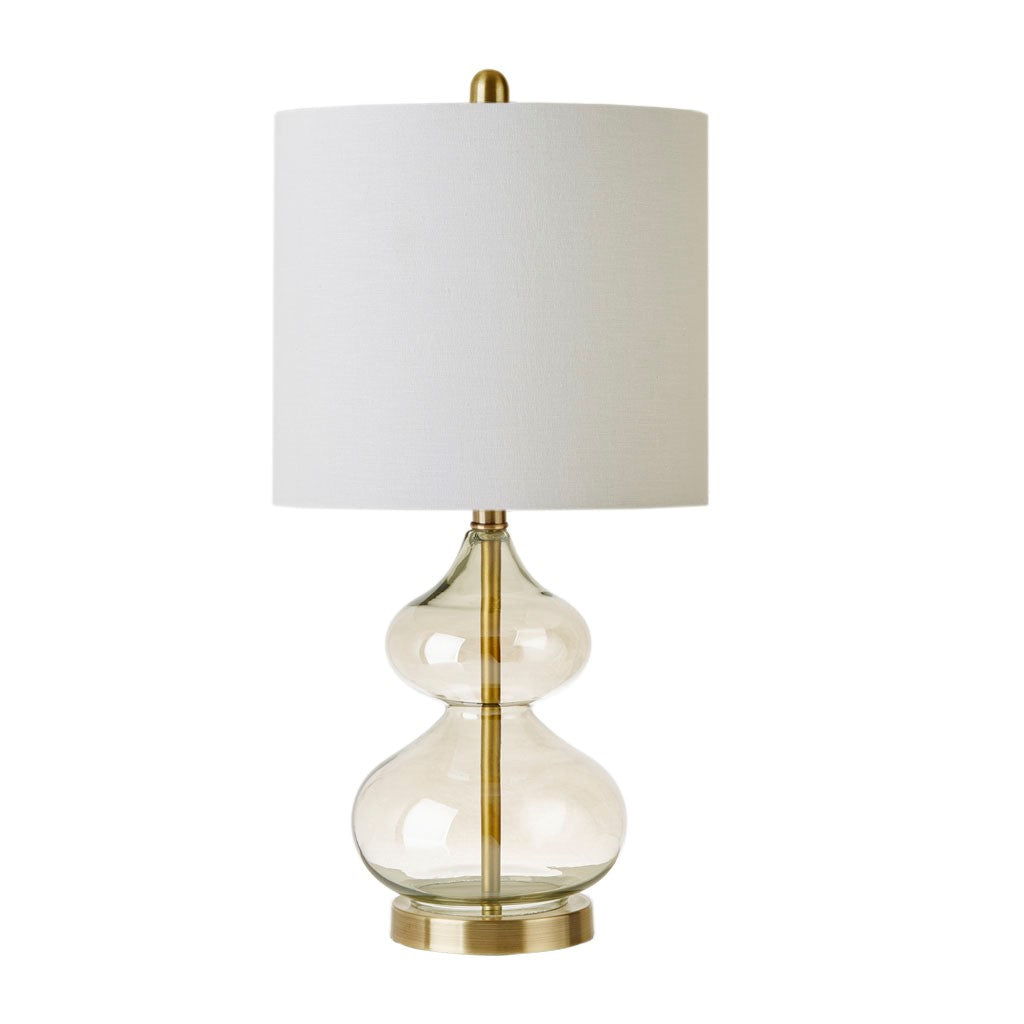 Table lamp with clear glass base, gold accents, and white shade on a white background