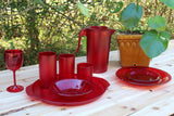 Red plastic tableware set on a wooden table outdoors with greenery in the background