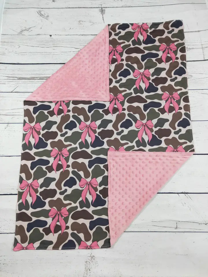 Blanket with camouflage pattern and pink bows on a wooden surface