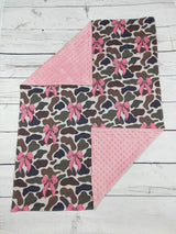 Blanket with camouflage pattern and pink bows on a wooden surface