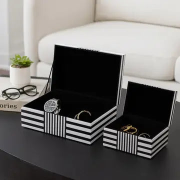 Black and white striped jewelry boxes with watches and rings on a table.