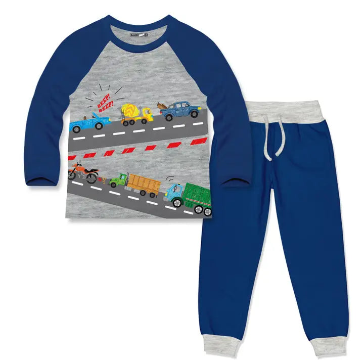 A two-piece children's pajama set featuring a long-sleeve raglan top and matching jogger pants. The top is heather gray with navy blue sleeves and a graphic print of cartoon trucks and cars on a road.