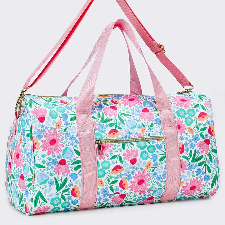 A duffle bag with a light blue and white floral print, pink handles and shoulder strap, and gold-tone hardware, shown on a light gray background.
