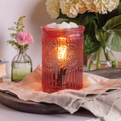 Decorative wax warmer with a lit candle on a table with flowers and plants in the background