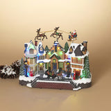 A festive miniature Christmas village figurine with snow-covered houses, glowing warm lights, a small bridge, evergreen trees, and Santa in a sleigh pulled by reindeer, displayed on a warm beige background.