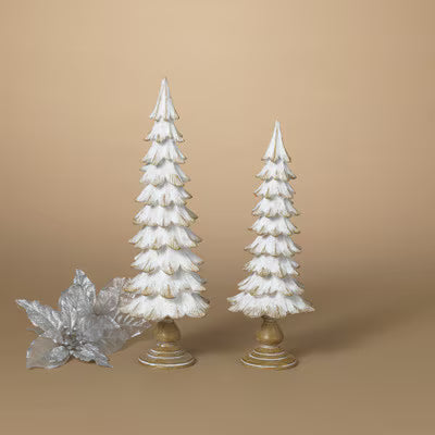 Two small white Christmas tree ornaments with gold bases, displayed on a warm beige background next to a silver decorative leaf.