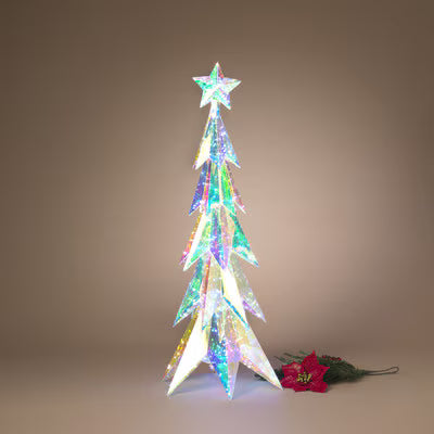 A decorative illuminated Christmas tree in a star-topped conical shape, covered in iridescent holographic material that shifts between green, blue, pink, and gold. It stands on a neutral warm brown background next to a red poinsettia stem.