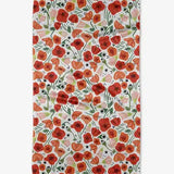A tea towel with a floral pattern featuring red and orange poppies, green leaves, and black accents on a white background.