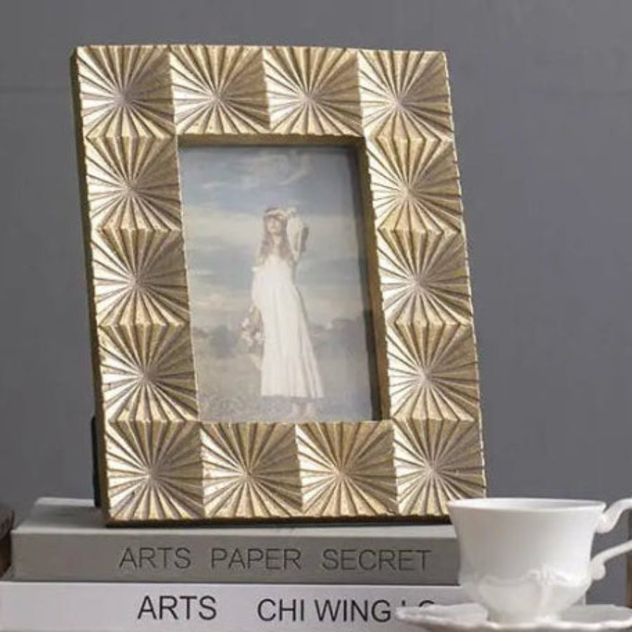 Decorative photo frame on a small table with a cup and saucer, against a gray wall.