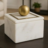 Marble box with a gold sphere on top in a blurred indoor setting