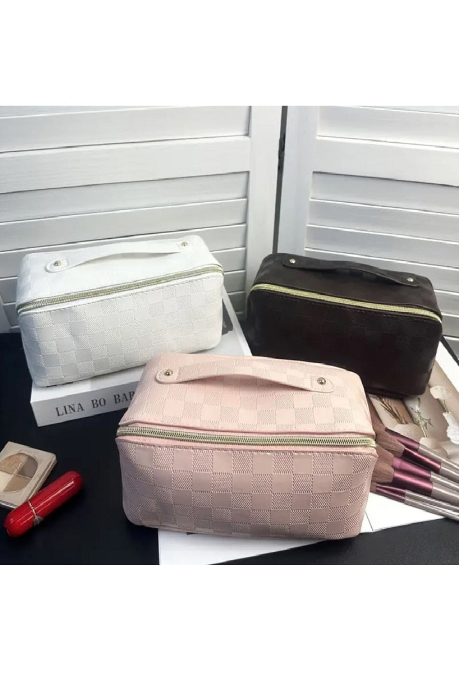 Three cosmetic bags one white one black one light pink on a surface with a white background