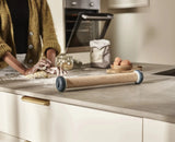 Wooden rolling pin on a kitchen counter with a person preparing food in the background