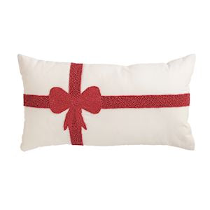 An off-white rectangular throw pillow featuring a red glittery ribbon and bow design printed across the front, set against a plain white background.