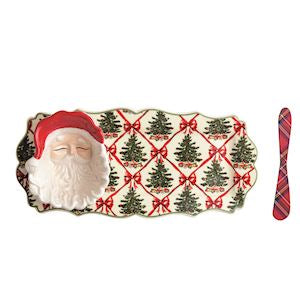 A Christmas-themed ceramic serving platter featuring a 3D Santa Claus figure on the left and a red-and-green plaid handle on the right, with a repeating pattern of green Christmas trees and red bows on a cream background.