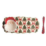 A Christmas-themed ceramic serving platter featuring a 3D Santa Claus figure on the left and a red-and-green plaid handle on the right, with a repeating pattern of green Christmas trees and red bows on a cream background.