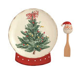A Christmas-themed ceramic plate or decorative dish on a red stand, shown next to a small Santa-shaped wooden spoon or spatula on a plain white background.