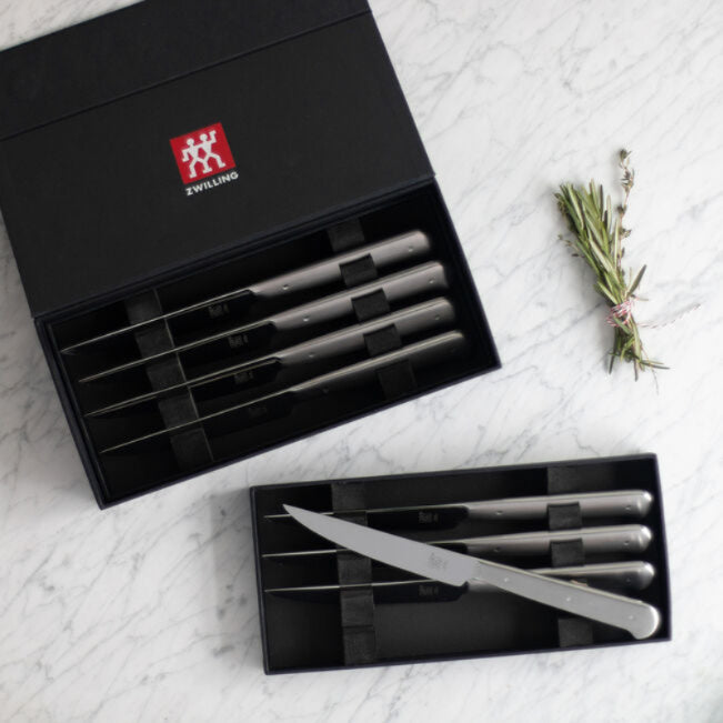 Set of knives in black Zwilling box on a marble surface with rosemary.