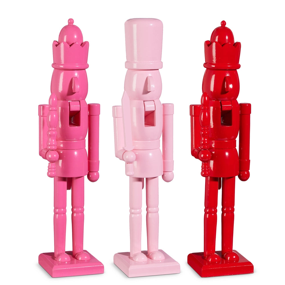 Three colorful nutcracker figurines in pink, red, and white on a white background