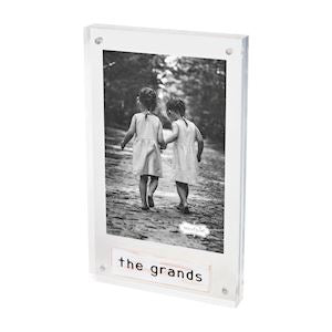 A clear acrylic picture frame with a black and white photo of two individuals and the text 'the grands' at the bottom.