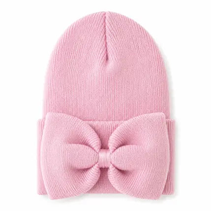 A light pink ribbed knit beanie hat featuring a large matching fabric bow attached to the folded cuff, shown on a plain white background.