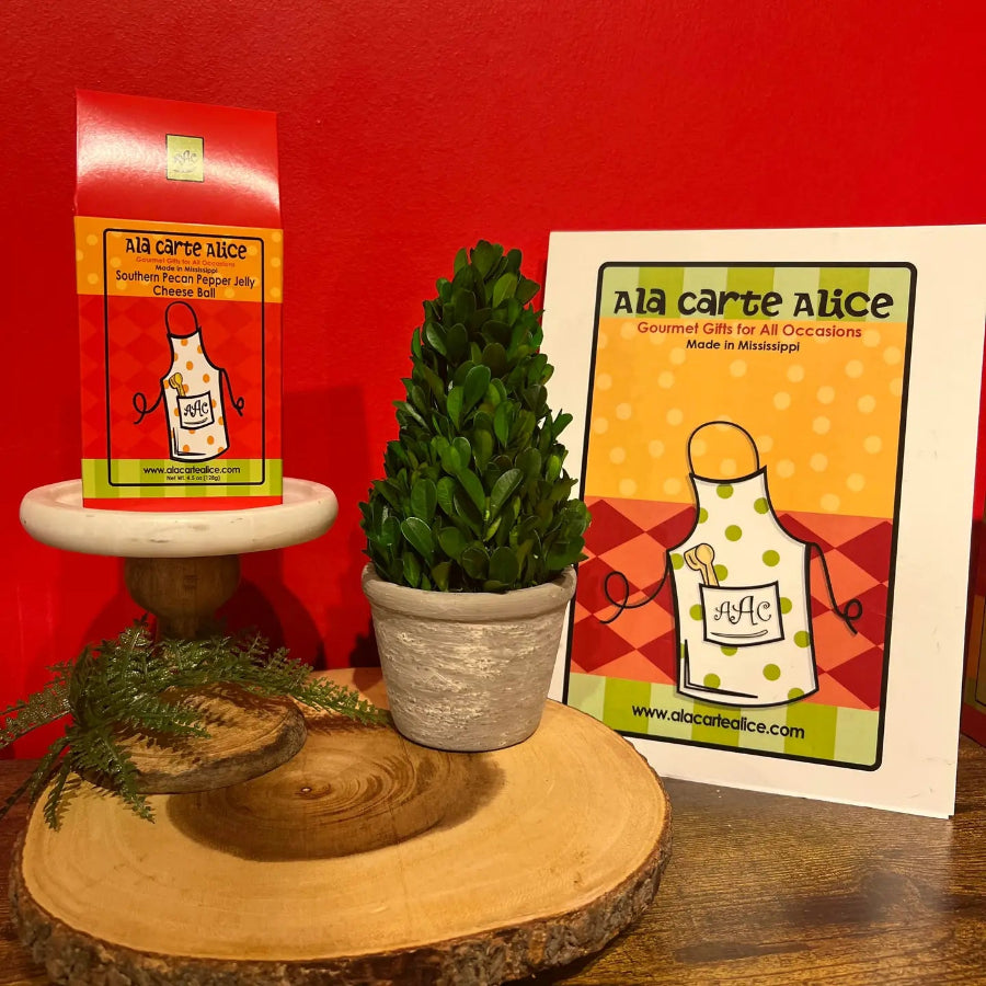 Potted plant on a wooden stand with 'Ala carte Alice' packaging and card against a red background