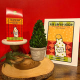 Potted plant on a wooden stand with 'Ala carte Alice' packaging and card against a red background