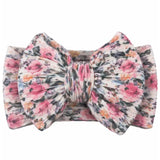 A fabric bow tie with a large bow and matching striped elastic band, featuring a watercolor-style floral pattern in pink, orange, and black on a cream background.