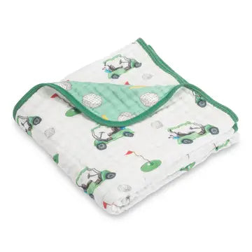 A folded white muslin baby blanket with a green and gray golf cart pattern, featuring a solid green reverse side and trim.