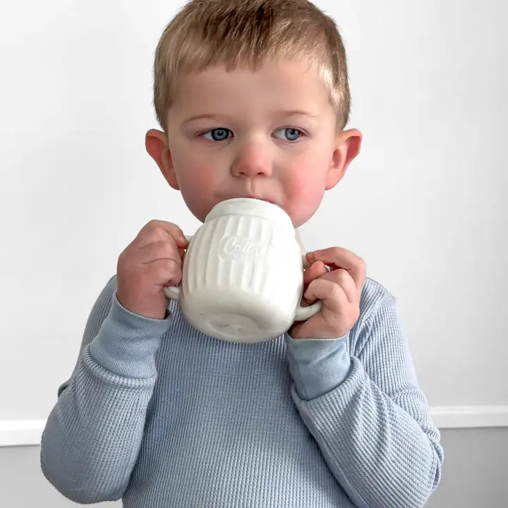 Child holding a white mug against a plain background