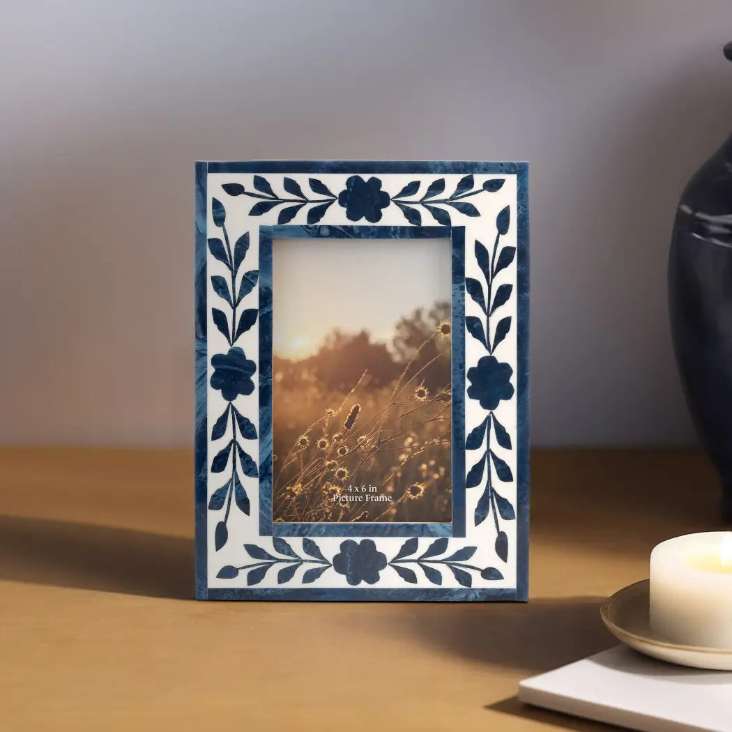 Decorative photo frame with floral patterns on a wooden surface with a candle in the background.