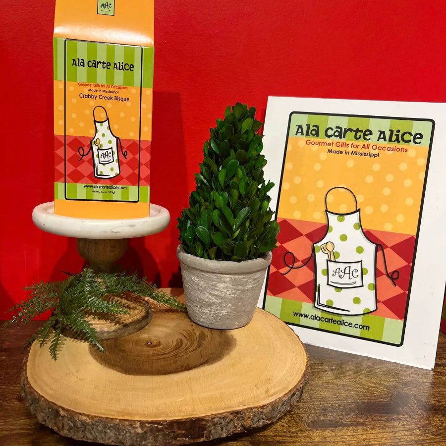 Potted plant on a wooden stand with 'Ala carte Alice' packaging and card in the background.