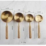 Set of four brass measuring spoons with wooden handles, shown with measurements on a marble background.