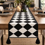 A black and white harlequin diamond-patterned table runner with black tassels, displayed on a wooden dining table set for four.