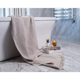 Beige textured blanket draped over a white bathtub with a candle and book on a marble surface.