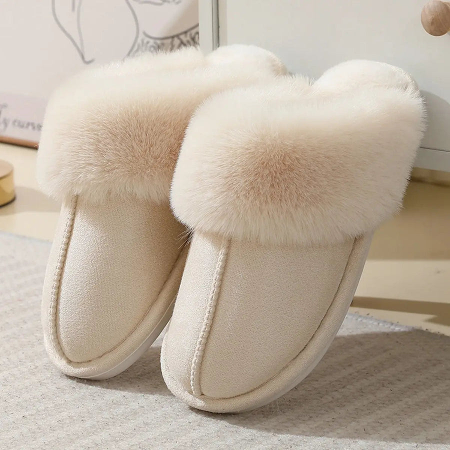 Pair of cream-colored slippers with fluffy pom-poms on a light background