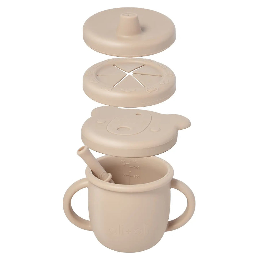 Beige sippy cup with multiple lids and a spoon on a white background
