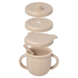 Beige sippy cup with multiple lids and a spoon on a white background