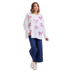 Woman wearing a white sweater with pink bow patterns and blue pants on a white background