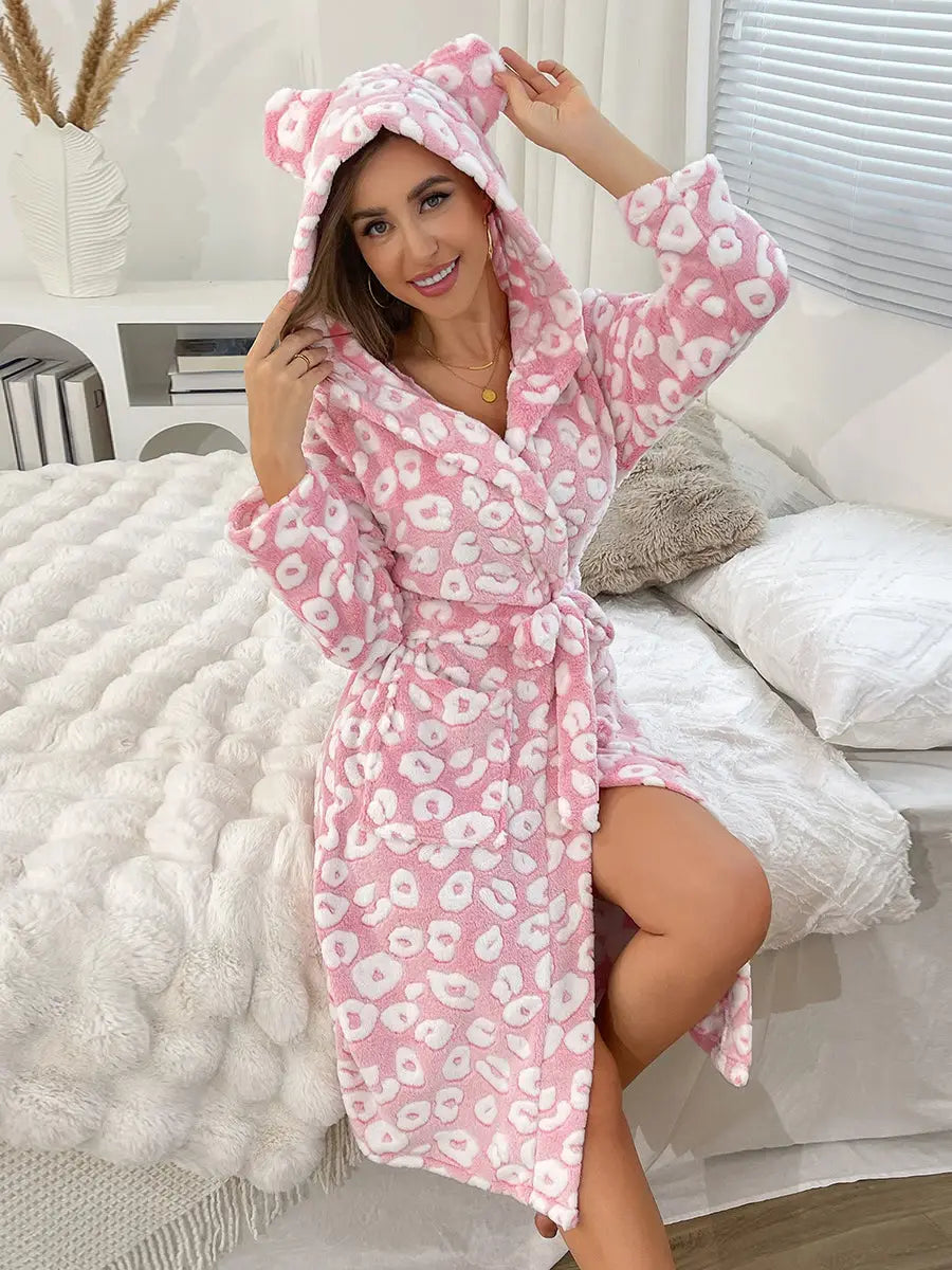 Woman wearing a pink leopard print robe with a hood in a bedroom setting.